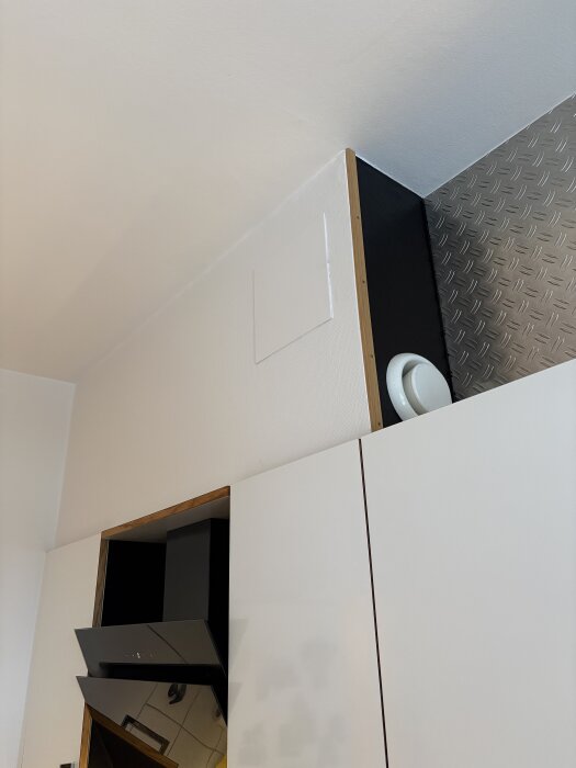 Köksfläkt med överskåp visar en ventilationskanal och en lucka i väggen vid taket, i en bostadsrätt som planerar köksrenovering.