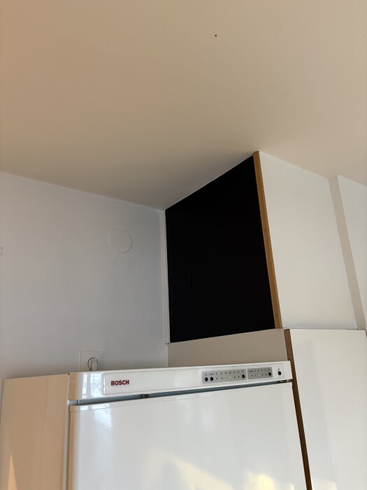 Överskåp ovanpå ett kylskåp med en svart låda eller ventilationshuv som når upp till taket i ett kök.