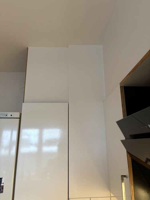 Kök med vita skåp och fläkt; synliga byggdetaljer vid taket som kan påverka överskåpens utformning, eventuellt för ventilation.