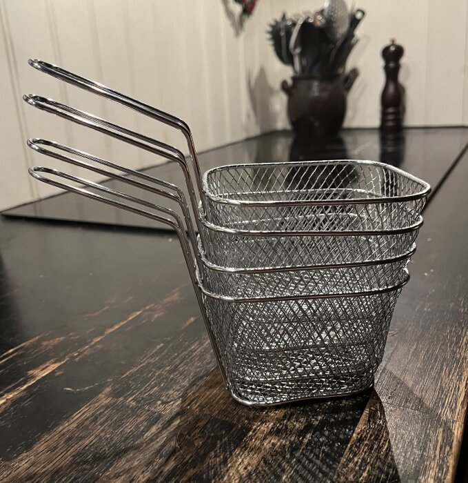 Fyra metallkorgar staplade i varandra på ett mörkt träbord, avsedda för servering av tillbehör som pommes frites.