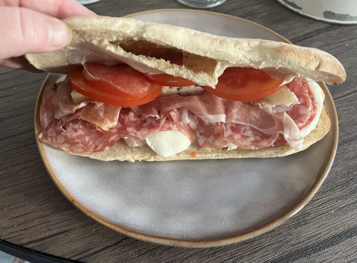 Italiensk smörgås med salami, serranoskinka, ost, mozzarella och tomater på tallrik.