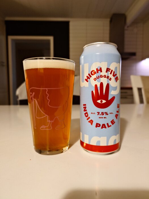 Ett glas med bärnstensfärgad öl och en burk Dugges High Five India Pale Ale på ett bord.