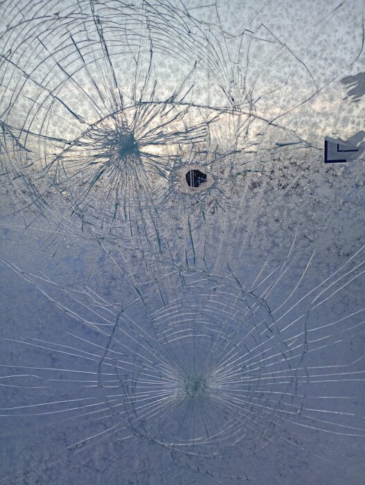 Sprucken glasskiva med flera cirkulära sprickor spridda över ytan, reflekterar omgivande ljus.