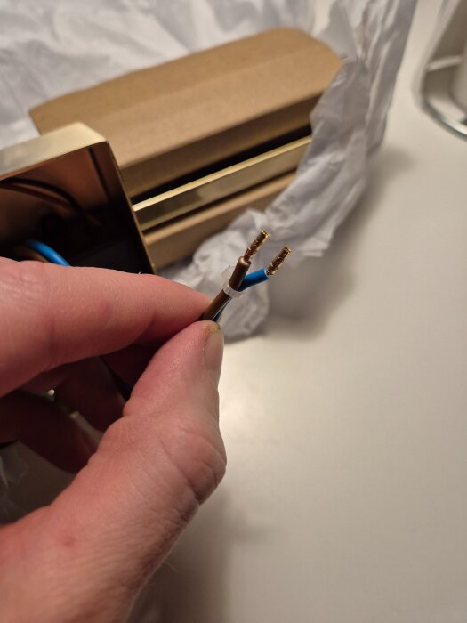 En hand håller två elektriska kablar med olika färgade höljen, troligen dubbelisolerade H03VH7-H-kablar.
