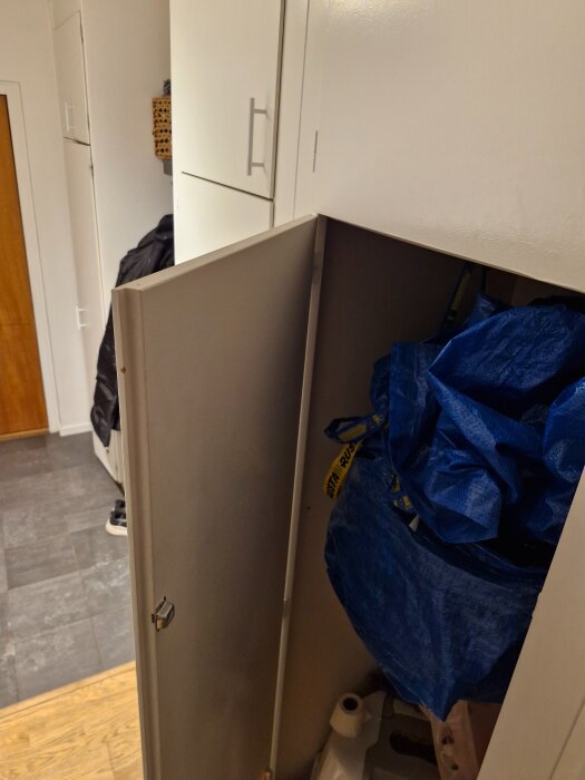 Öppen vit garderobsdörr i hall, med blå IKEA-kasse och verktyg inuti.