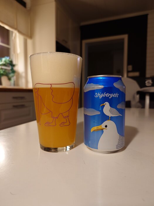 Ett ölglas fyllt med skummande öl bredvid en ölburk med måsmotiv, placerade på ett vitt bord i ett kök.
