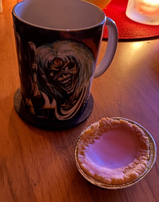En tom mazarinform bredvid en mugg med ett tryck av en skräckfigur på ett bord.