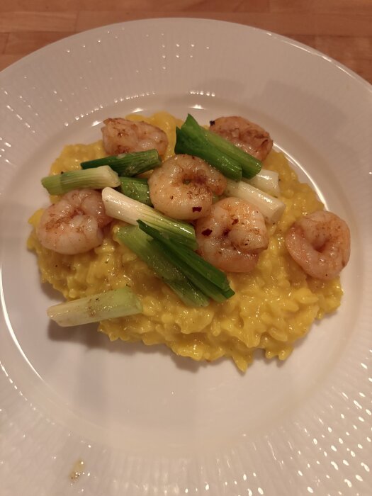 Tallrik med saffransrisotto toppad med räkor och salladslök.