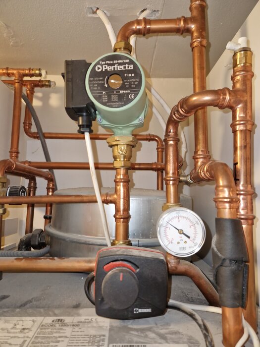 Cirkulationspump för uppvärmning med kopparrör och termometer, fokus på pumpdetalj och rörsystem.