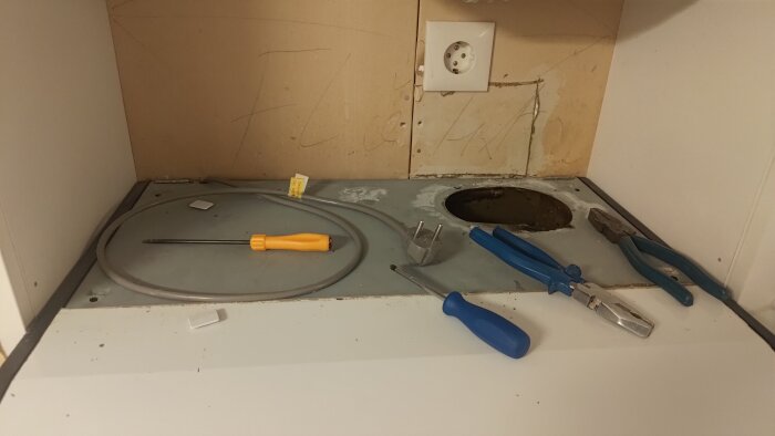 Verktyg och elektriska komponenter på en köksbänk; en orange och en blå skruvmejsel, en kabel med kontakt, tång, hål där fläkt suttit.