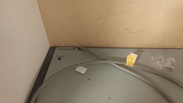 Metallplåtar och en kabel ovanpå en köksfläkt, med väggen i bakgrunden. En etikett med text syns på fläktens yta.