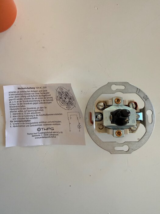 Instruktionsblad och en ny strömbrytare på ett bord, för byte av elektrisk installation, med skruvanslutningar synliga.