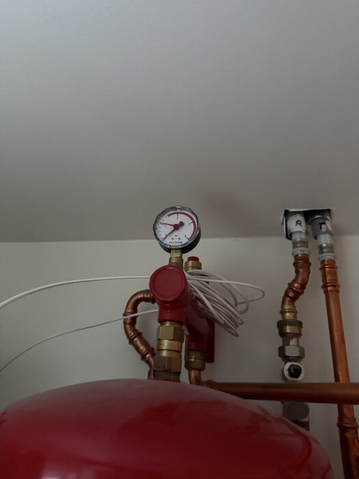 Tryckmätare och rörinstallation med kopparrör och en röd expansionskärl.
