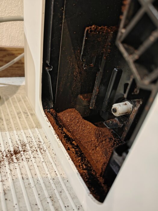 Kaffesump i en kaffemaskinsavfallslåda, med spill på en randig yta vid sidan om.
