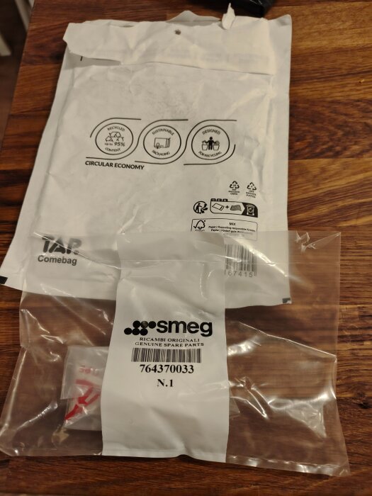 Plastpåse med Smeg reservdelar på träbord och kuvert märkt med återvinningssymboler.