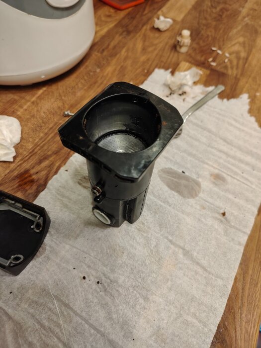 Montering av en svart metalldel på en trären bänk, omgiven av verktyg och papper.