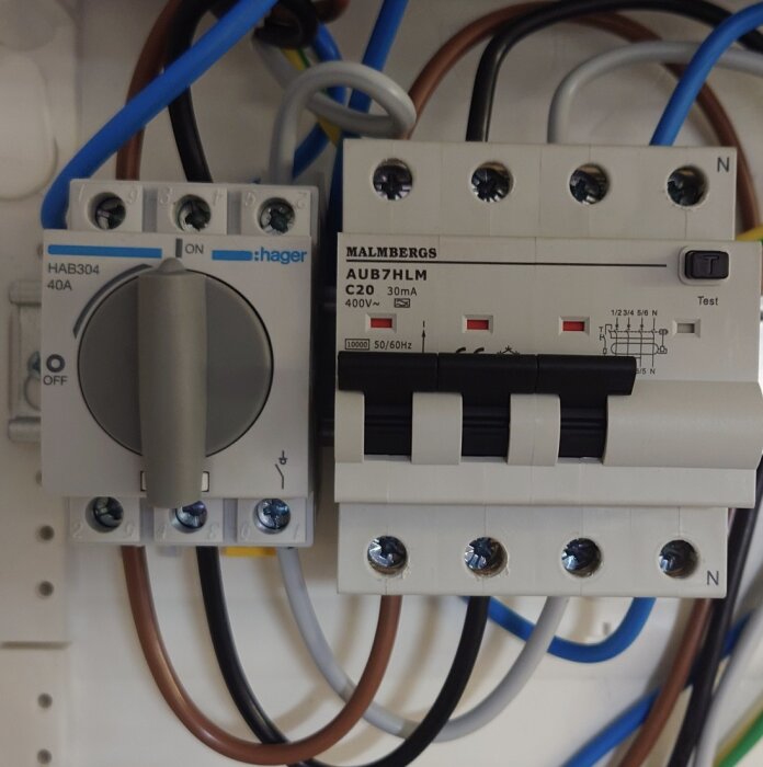 Närbild av en elinstallation med en Hager strömbrytare och en Malmbergs strömbrytare med anslutna kablar, inklusive gula ändhylsor.