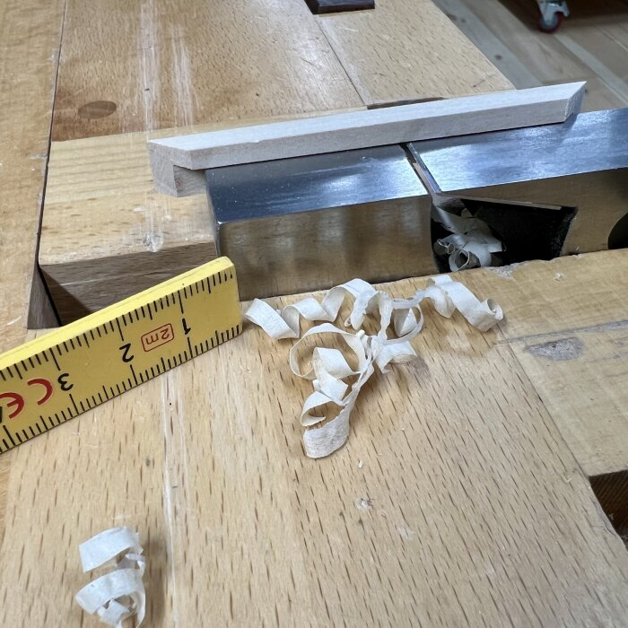 Träbänk med hyvelspån vid en elhyvel samt en linjal för mätning.