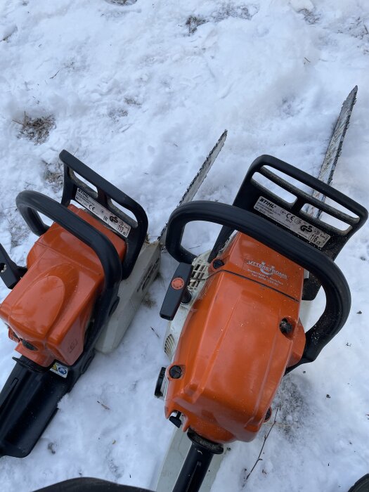 Två orange motorsågar ligger på marken i snön, redo att användas efter att ha kapat av fallna tallar över en skogsväg.