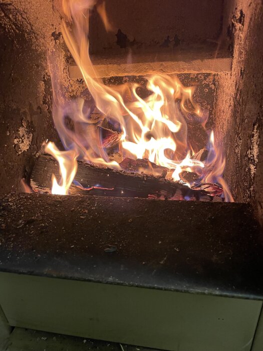 Brasa i vedpanna, med lågor och brinnande ved, i skogsmiljö vid kallt väder.