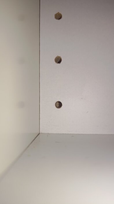 Hål i en vit skåpsvägg för hyllplan, inga dolda skruvar synliga. Fläktinstallation mot sidoskåp.