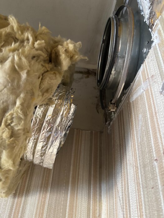 Isolerad imkanal och stos mot murstock med synlig aluminiumslang och isolering. Ventilationsinstallation hemmavid.