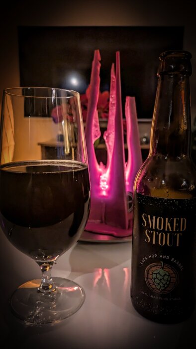 Glas och flaska med Smoked Stout-öl på ett bord, med ett lila ljus i bakgrunden.