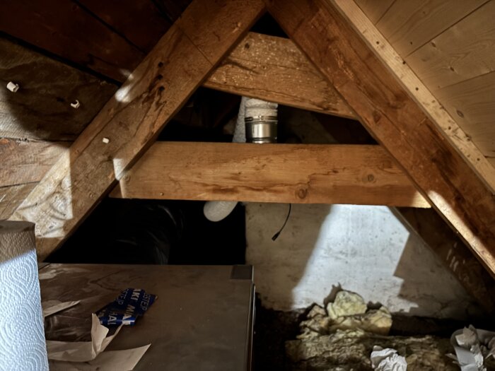 Råvind med träbjälkar, isolering synlig på golvet och rör i metall installerat mellan trästöd.