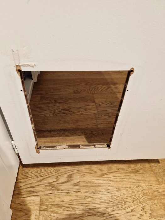 En utskuren del av en dörr visar insidan med två tunna MDF-skivor och kartong emellan, med öppning mot ett trägolv.