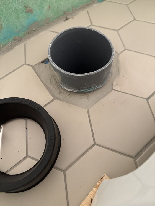 Ett rörrör och en muff som används i ett byggprojekt, placerade på ett golv med sexkantiga plattor.