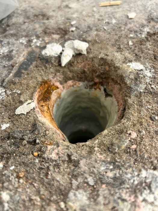 Närbild av ett borrat hål i en betongyta, omgiven av sprickor och smuts.