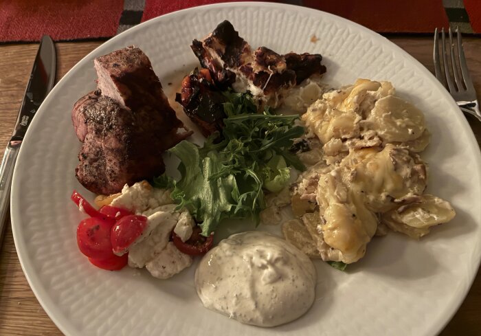 Grillad fläskytterfilé med potatis- och tryffelgratäng, tomat- och mozzarellasallad, småpaprikor, halloumi, sallad och kall bea-dipp på tallrik.