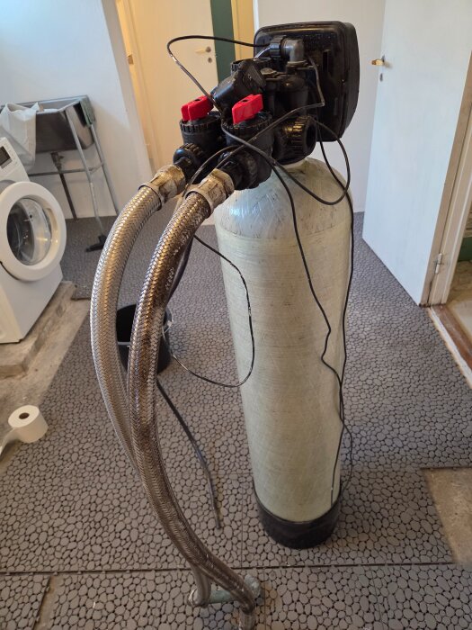 Utkopplat Erie vattenfilter model No. 1044 med metallrör och kablar i ett tvättrum.