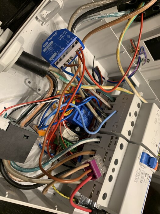 En elsäkringsbox med flera kablar och en Shelly-enhet installerad i ett vägguttag.