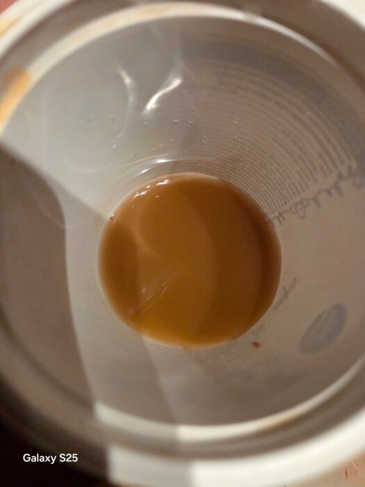 Brunt, rostfärgat vatten i en plastkopp, troligtvis från rensning av radiatorens termostat.