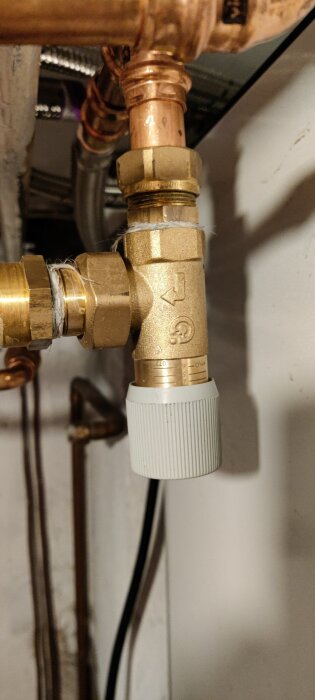 Ventil och kopparrör i ett värmesystem, potentiellt en shuntventil, med plastvred längst ner och pilmarkering på ventilen.