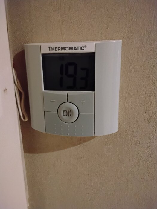 Rumsgivare med digital display som visar temperatur 19.3, av märket Thermomatic. Knappar för manövrering syns under displayen.