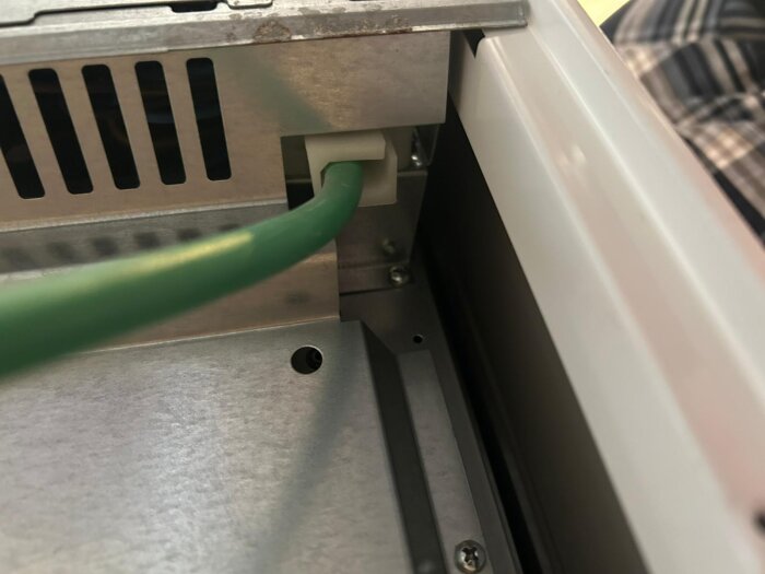Grön elkabel inkopplad i en metallisk kopplingsdosa på baksidan av en spis.
