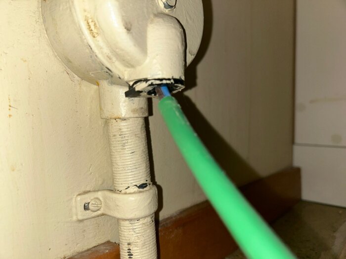 Grön elsladd i en fast ansluten elinstallation vid väggen, nära golvlist.