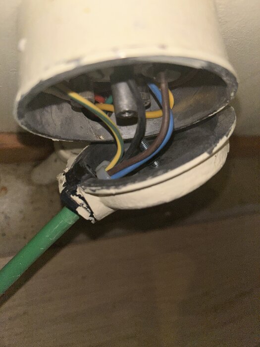 Öppen elbox med flera synliga färgade kablar i ett vägguttag, inklusive gröngul, brun och blå kabel, samt en grön slanganslutning.