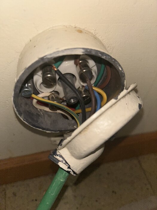Elektrisk kopplingsdosa på vägg med flera färgade kablar anslutna och en öppnad lock, visar insidan av installationen.