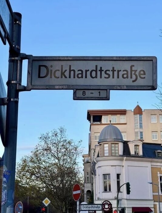 Gatuskylt med texten "Dickhardtstraße" i Berlin, flankerad av ett träd och en byggnad under klarblå himmel.