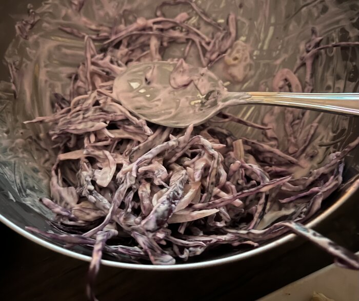 Lila coleslaw av rödkål i en metallskål med sås, en sked ovanpå röran.