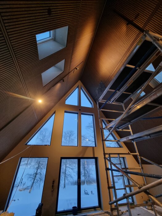 Interiör av ett nästan färdigställt tak med takfönster och stort fönsterparti, byggnadsställningar syns i förgrunden.