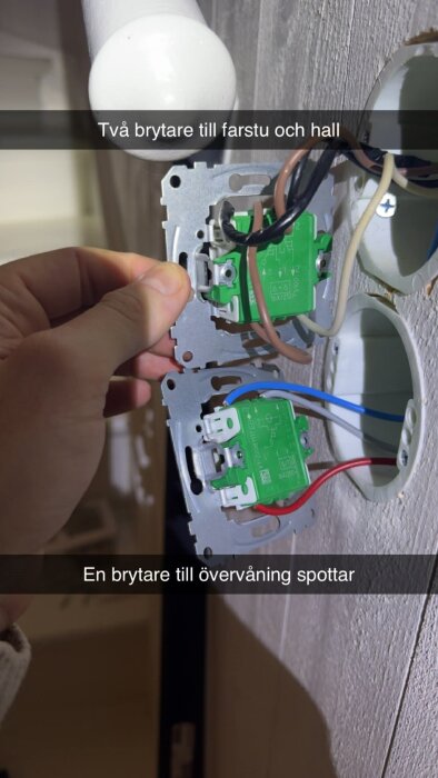 Hand monterar två elektriska brytare i en vägg med synliga kablar.