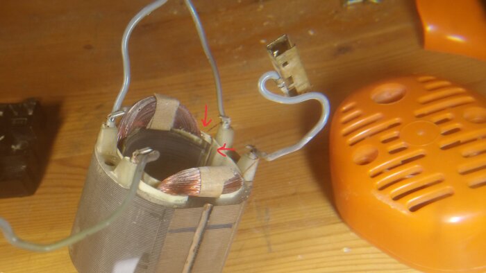 Kompakt elektrisk motor med lösa kopparkablar och anslutningar, placerad på ett träbord bredvid en orange plastdetalj.