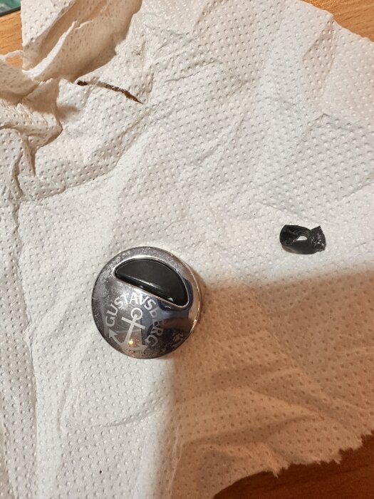 Förkromad Gustavsberg-knopp på hushållspapper, nära en liten svart del.