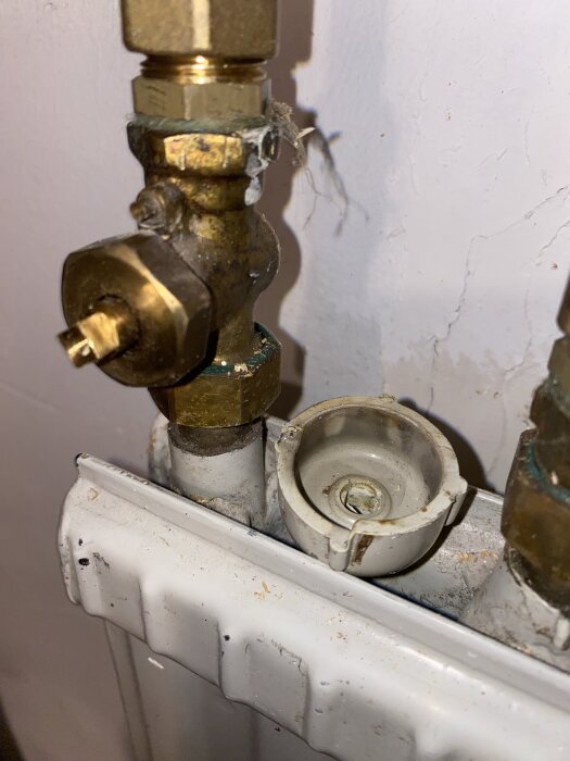 Vridventil och radiatorkoppel med monterad insats, del av vattenburet uppvärmningssystem, bakgrund av vit vägg och radiator.