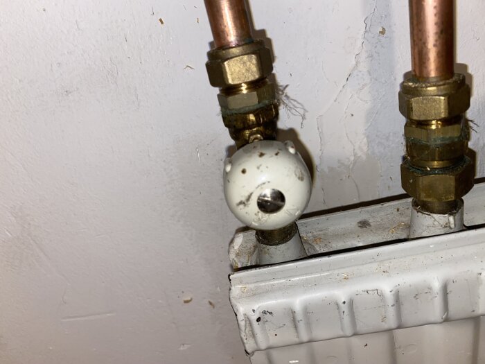 Vitt vridventilhuvud på en radiator med kopparrör och mässingskopplingar, monterat uppochner i ett gammalt uppvärmningssystem.