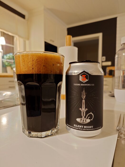 En glas med stout och en burk märkt "Silent Night" från 3 Sons Brewing Co. står på ett bord i ett kök.